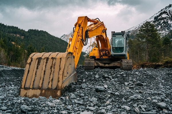 a yellow excavator is sitting on top of rocks.